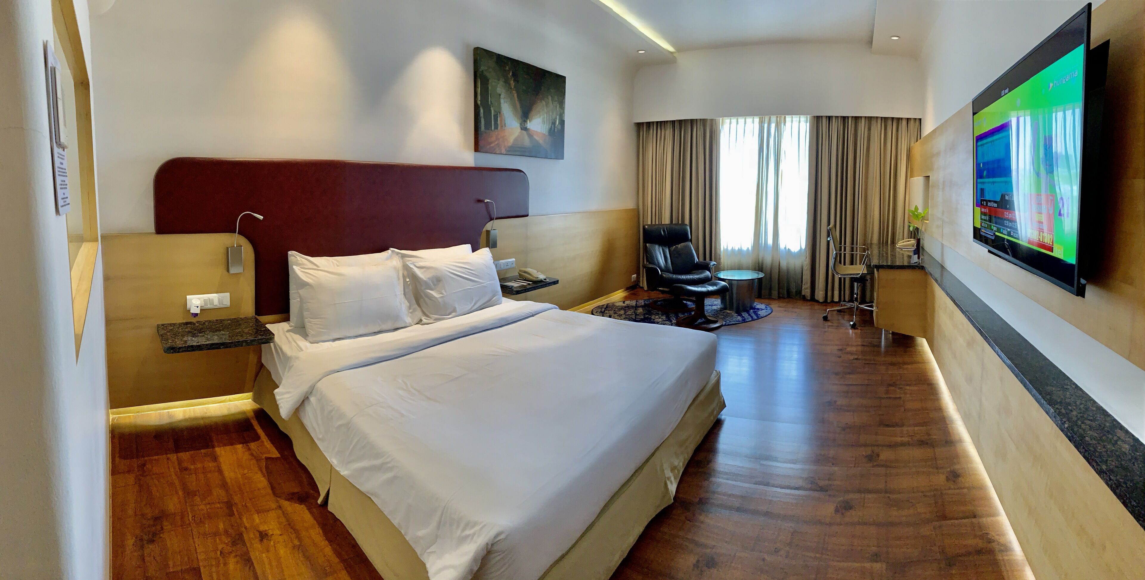 A hotel room with a large bed, a desk, a chair, a TV, and a window with curtains.