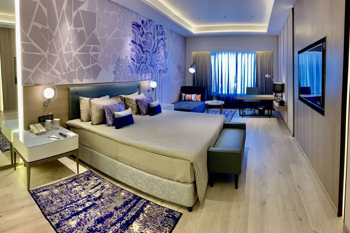 Une chambre d’hôtel moderne avec un grand lit, des tables de chevet, un bureau et une télévision.