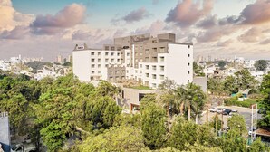 A multi-story hotel with a modern architectural design, surrounded by lush greenery and other buildings in the background.