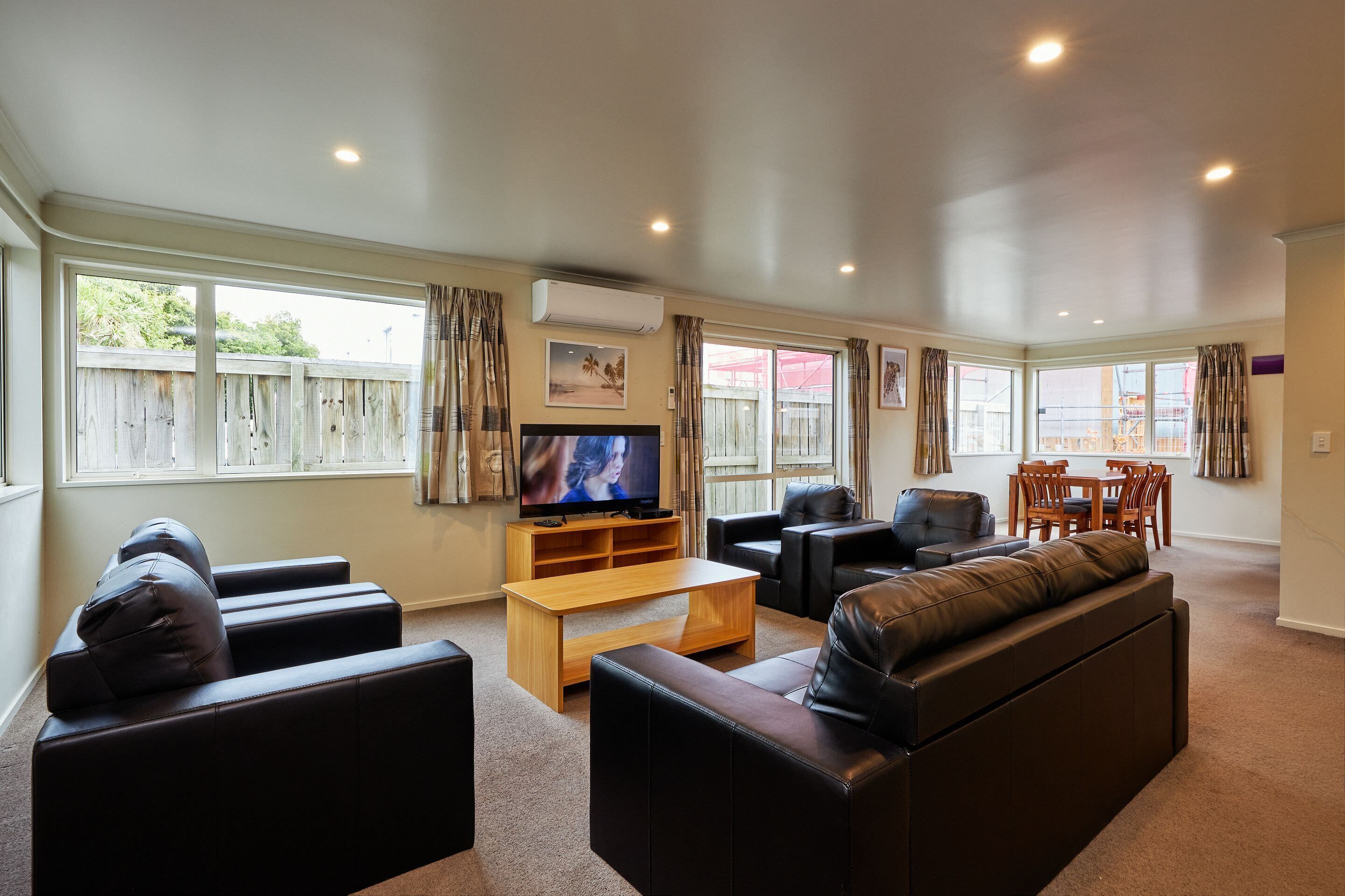 A spacious living room with a large TV, leather sofas, a wooden coffee table, and a dining area with chairs and a table.