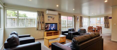 A spacious living room with a large TV, leather sofas, a wooden coffee table, and a dining area with chairs and a table.