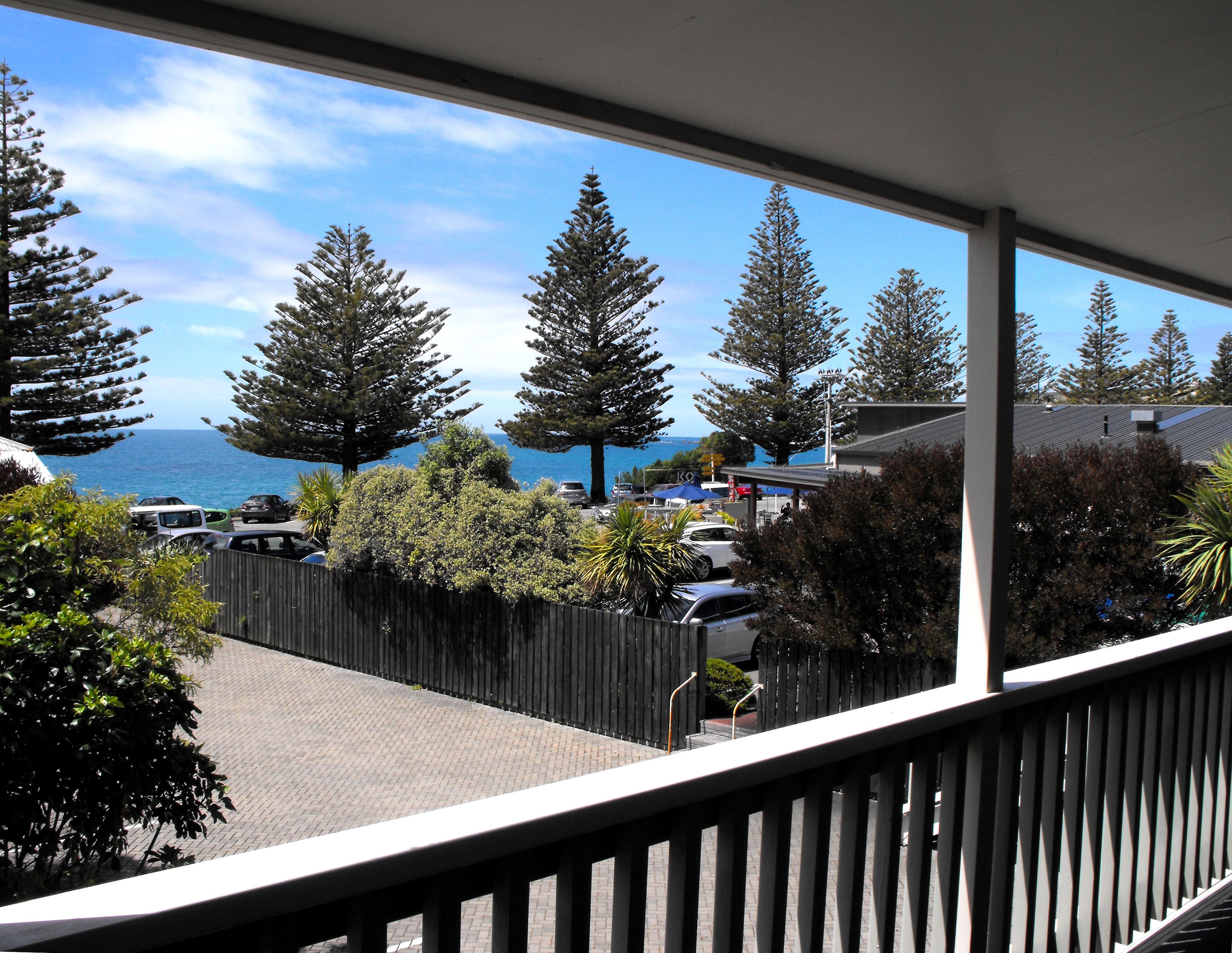 A balcony with a view of the sea, trees, and parked cars.