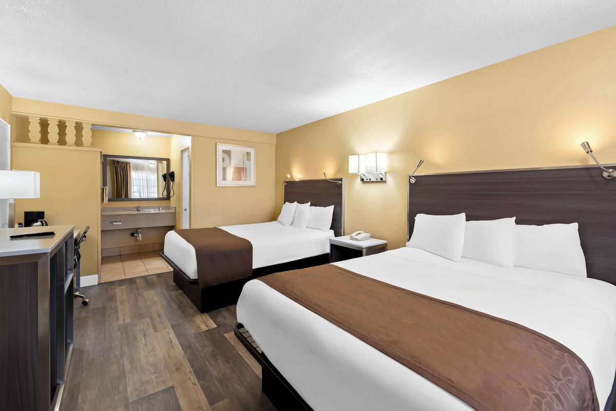 A hotel room with two beds, a desk, a vanity, and a mirror.