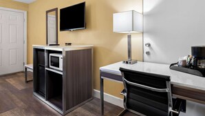 A hotel room with a desk, chair, TV, and a minibar. - Americas Best Value Inn & Suites Flagstaff (Flagstaff)