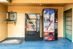 Máquina automática de bebidas com uma bebida tropical e outra máquina de snacks ao lado de uma porta.