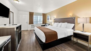 A hotel room with a bed, bedside table, lamp, TV, and a desk with a chair. - Americas Best Value Inn & Suites Flagstaff (Flagstaff)
