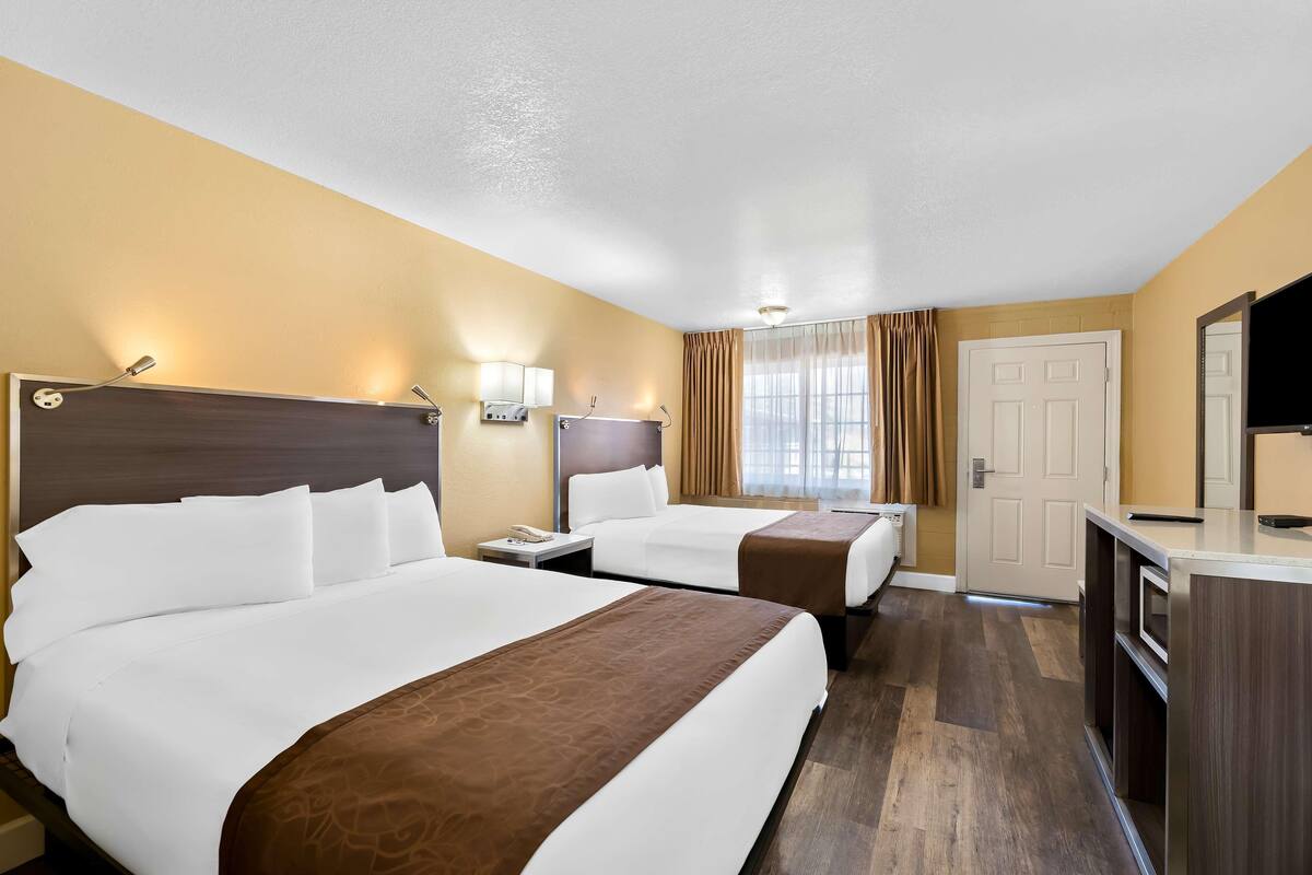 A hotel room with two beds, a desk, a TV, and a door.