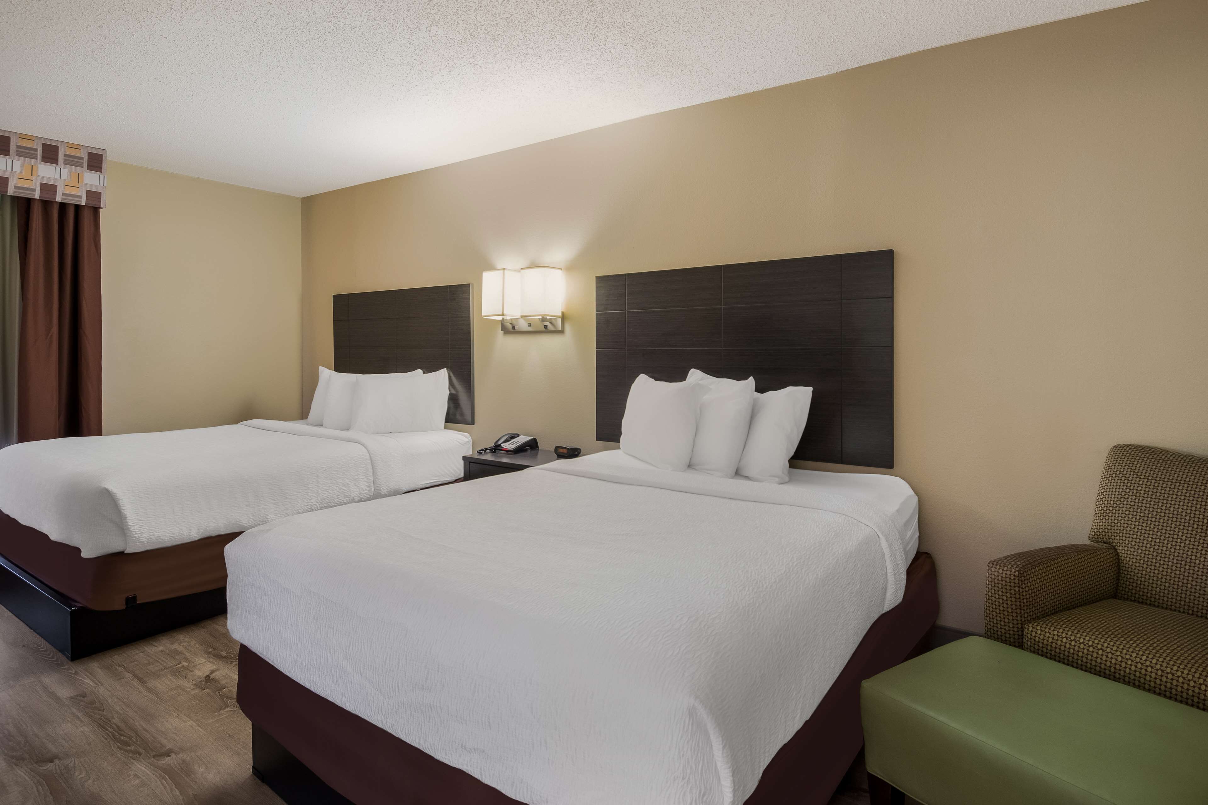 A hotel room with two beds, a nightstand, a lamp, and a green armchair.
