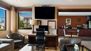 A hotel room with a desk, two chairs, a TV, a window with a view of buildings, and a kitchenette. - SureStay Plus Hotel by Best Western Jackson (Jackson)