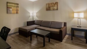A modern living room with a sectional sofa, a small table, and two wall-mounted lamps. - SureStay Plus Hotel by Best Western Jackson (Jackson)