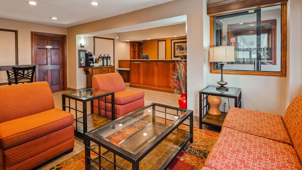 A hotel lobby with orange sofas, a glass coffee table, a red vase, and a wooden reception desk. - SureStay Plus Hotel by Best Western Jackson (Jackson)
