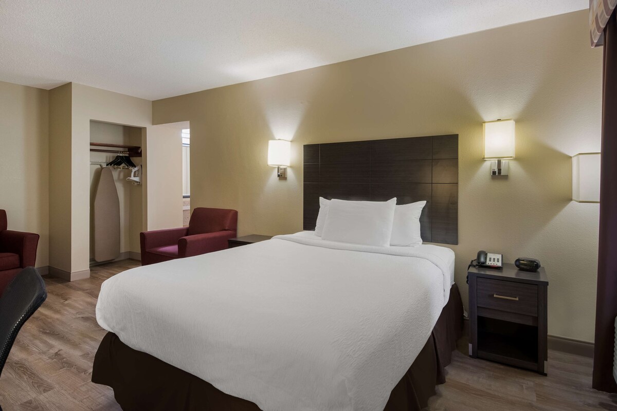 A hotel room with a large bed, two bedside lamps, a small bedside table with a phone, and a chair.