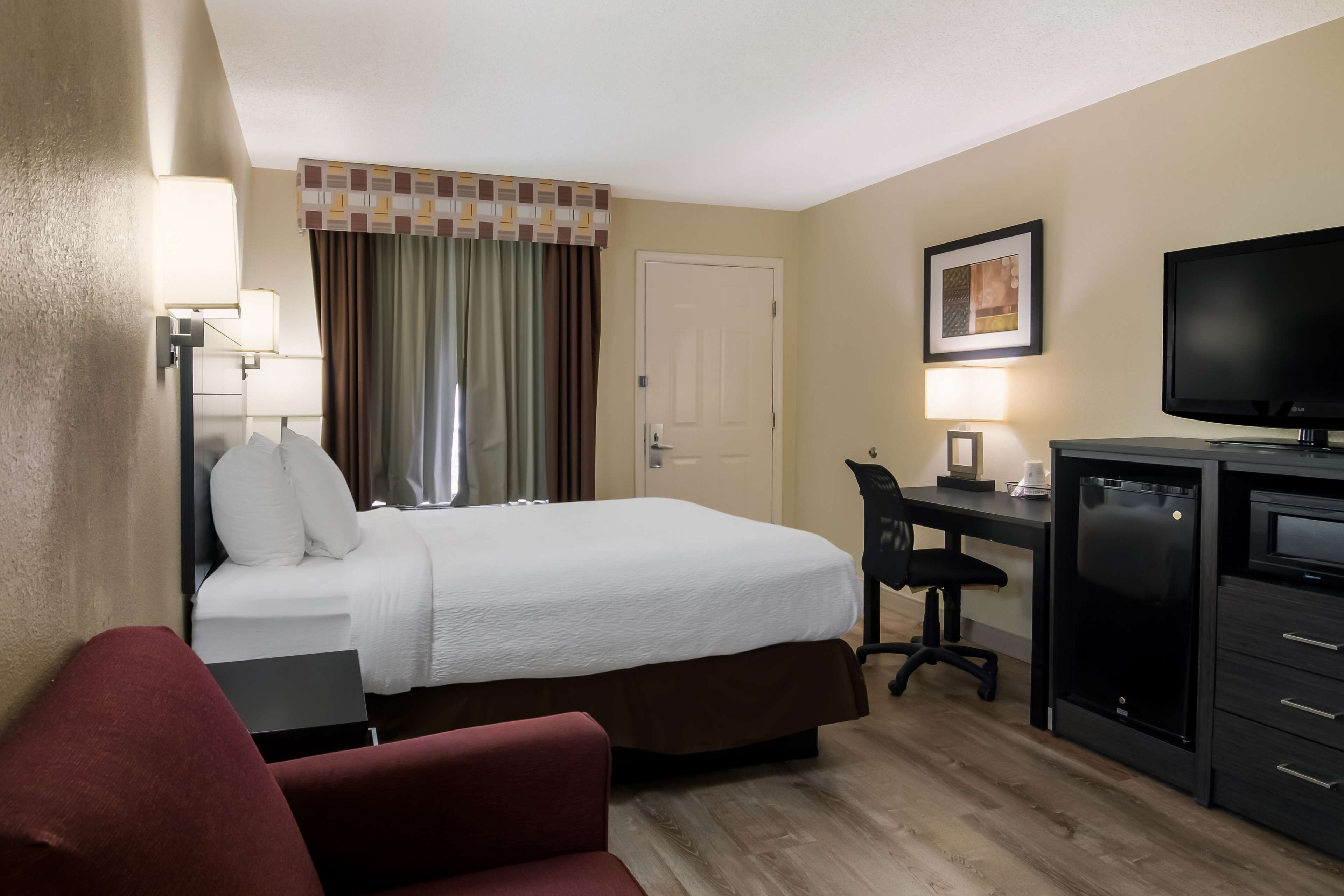 A hotel room with a bed, desk, chair, TV, and a minibar.