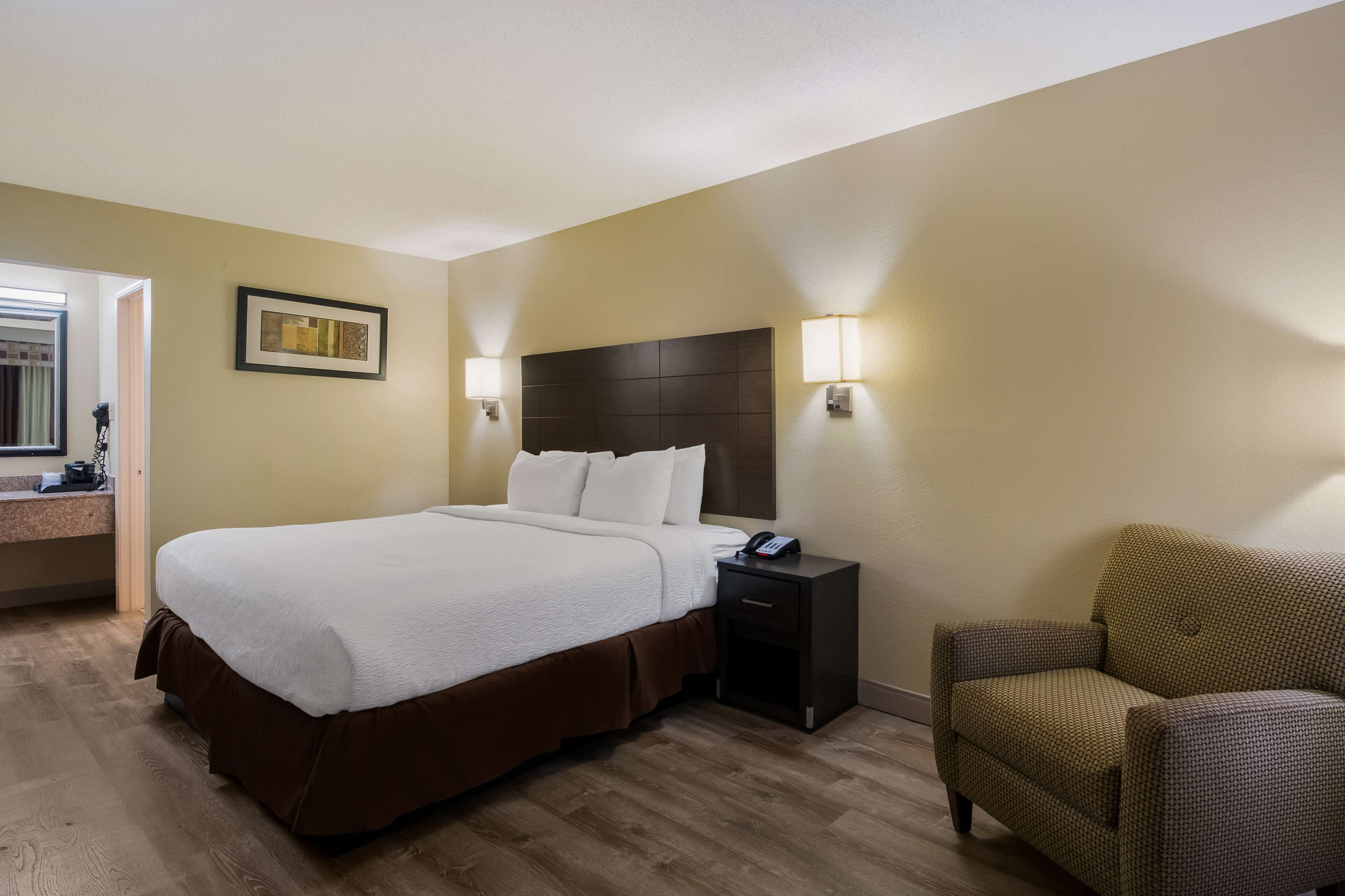 A hotel room with a large bed, a nightstand, a chair, and two wall-mounted lamps.