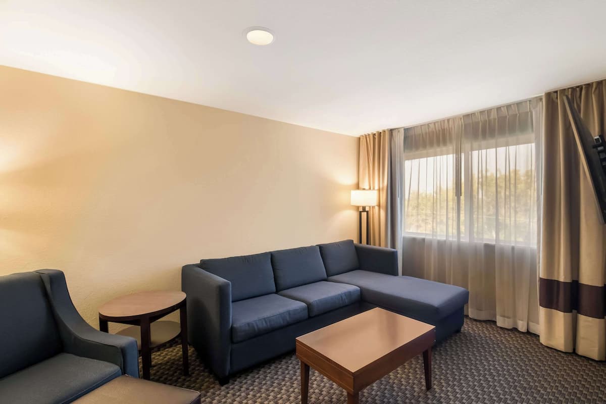 A hotel room with a sofa, two armchairs, a small table, and a lamp.