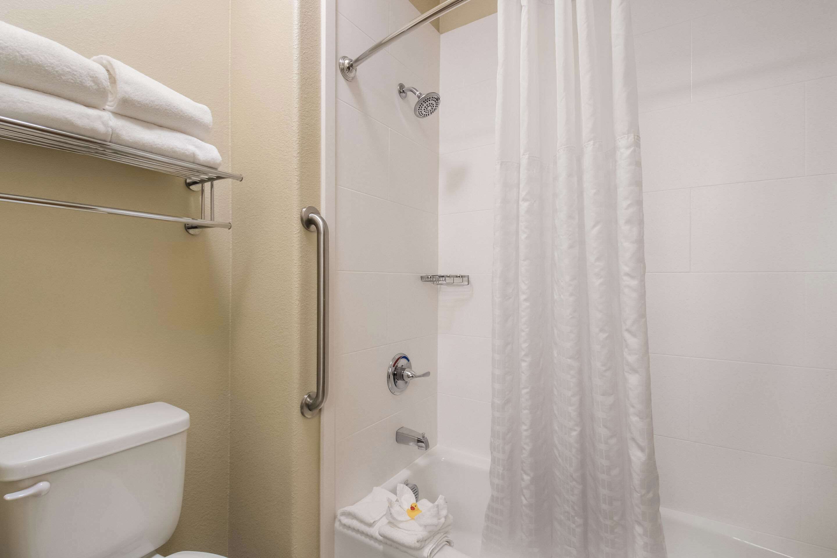 A bathroom with a toilet, a shower with a glass door, and a towel rack with folded towels.
