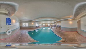 Una piscina interior con las normas de la piscina claramente expuestas en la pared, una silla de socorrista y una zona junto a la piscina con sillas de descanso.