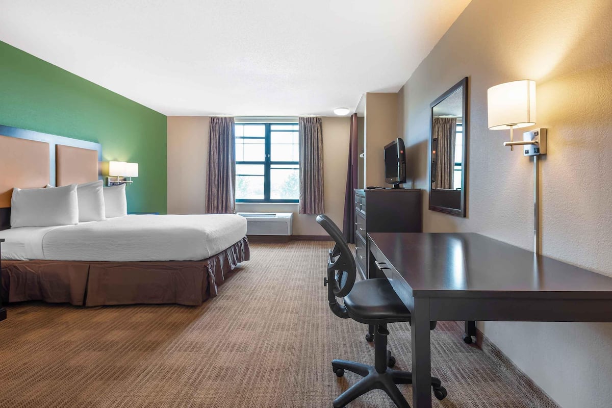 A hotel room with a bed, desk, chair, TV, and a window with curtains.