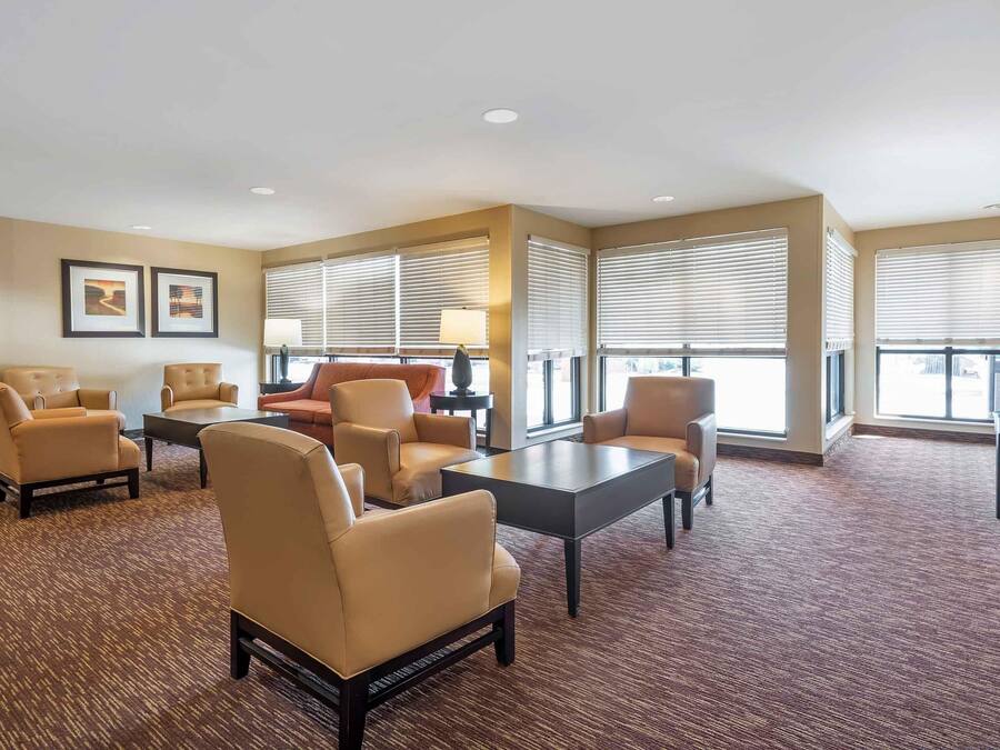 Un hall d’hôtel avec des canapés de couleur beige, une table basse et de grandes fenêtres équipées de stores.