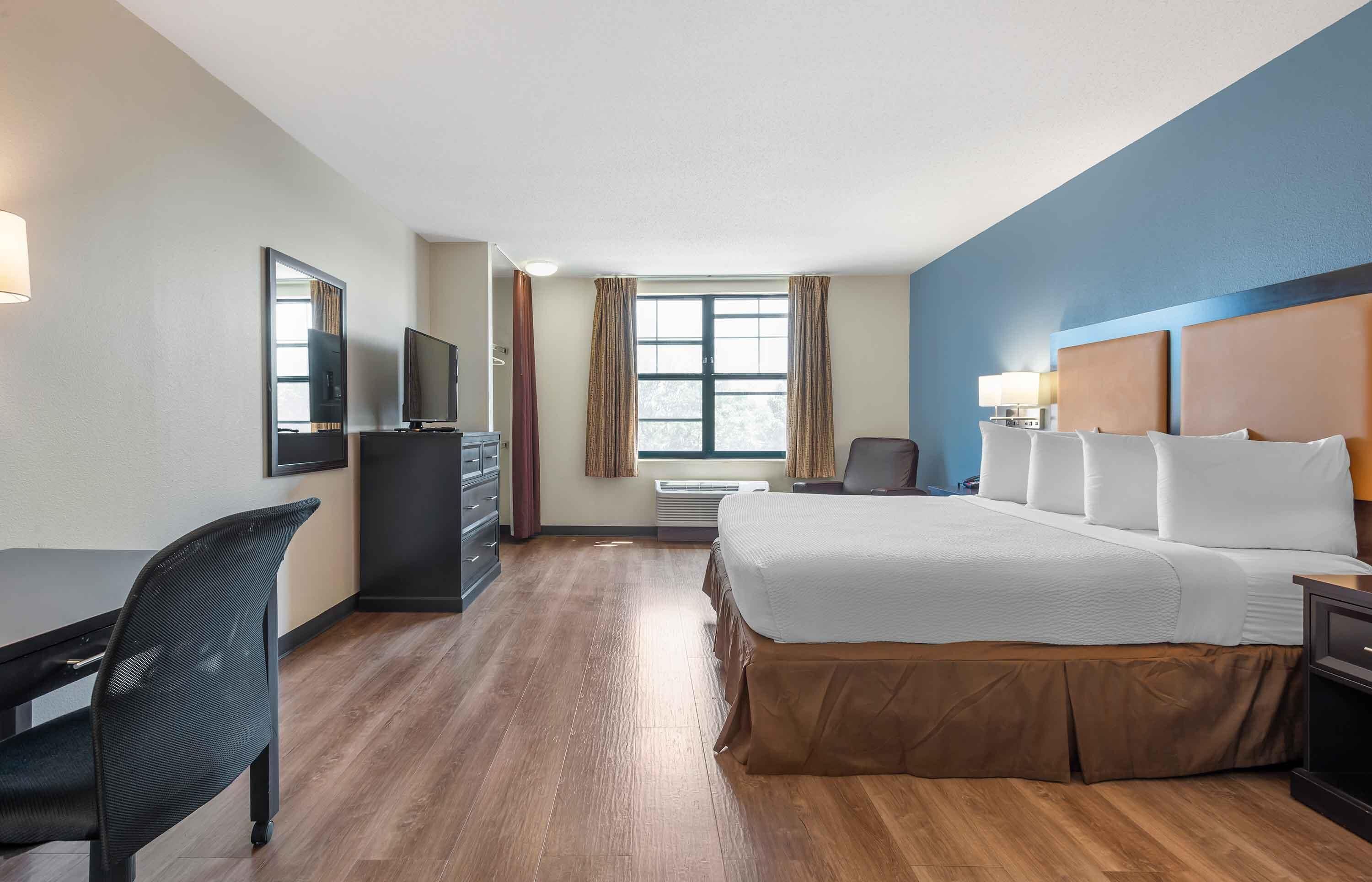 Una camera d'albergo con un letto grande, una scrivania, una sedia, una televisione e una finestra con tende.