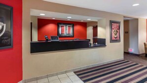 A hotel reception area with a black reception desk, a framed picture above it, and a red wall.