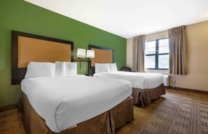 Ein Hotelzimmer mit zwei Betten, einer grünen Wand, einem großen Fenster mit Vorhängen und einem Kopfteil mit Lampen.