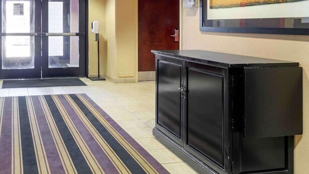Eine Hotellobby mit Streifenmuster-Teppich, einem schwarzen Schrank, einer Tür und einer wandmontierten Leuchte.