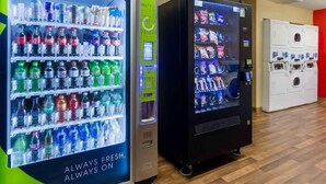 Zwei Getränke- und Snackautomaten sowie eine Waschmaschine in einem Raum mit Holzboden.