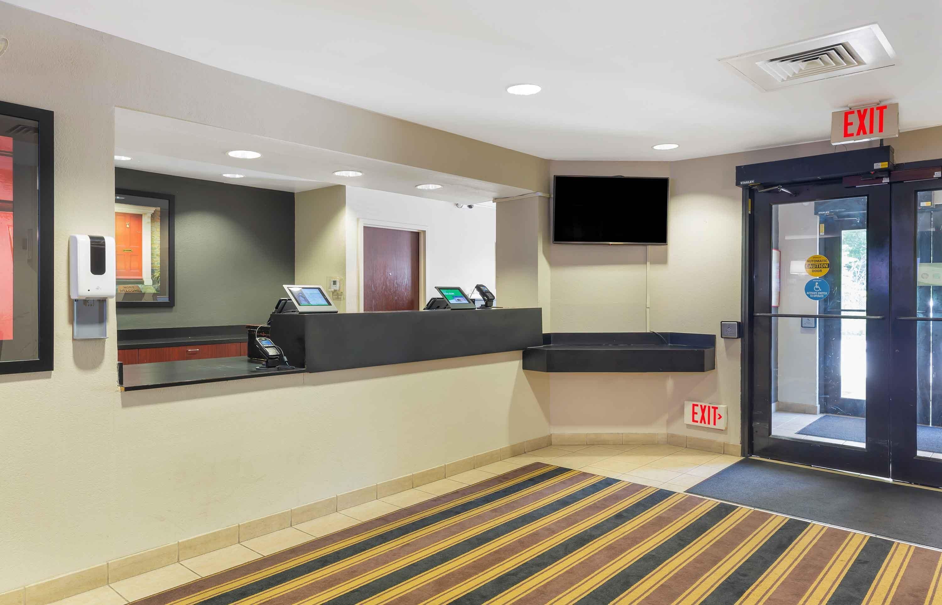 En hotellobby med en receptionsdisk, en dator, en telefon och en utrymningsskylt.