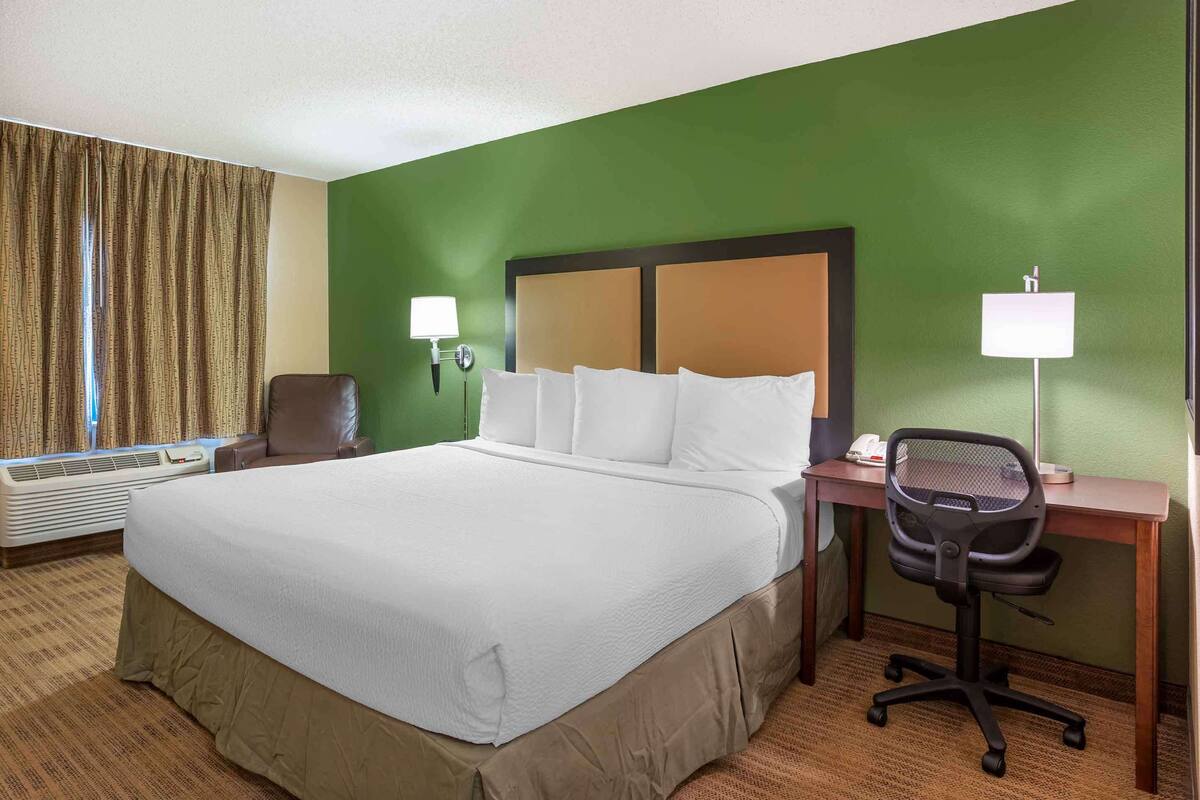 Una habitación de hotel con una cama grande, un escritorio con silla, una lámpara de pie y una ventana con cortinas.