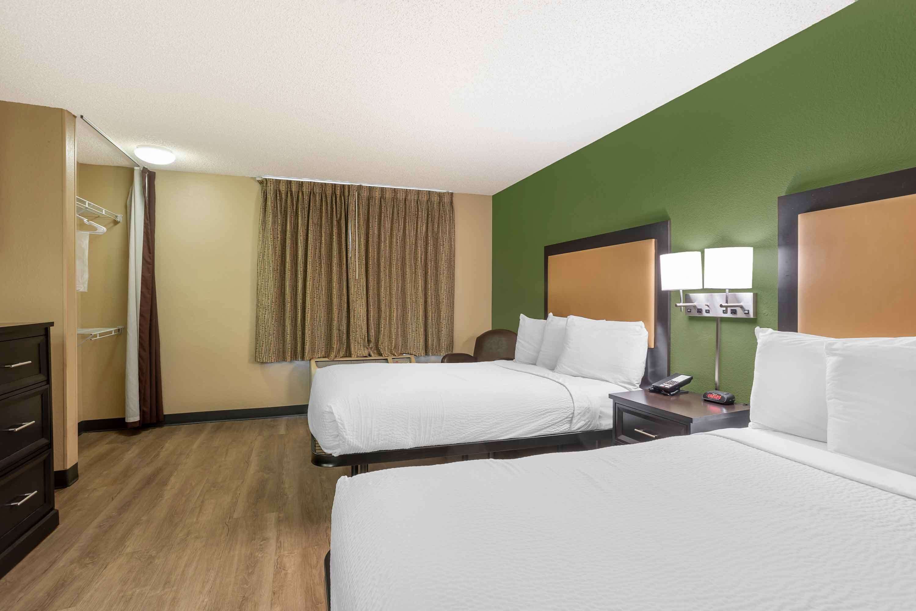 A hotel room with two beds, a desk, a chair, a lamp, and a mirror.