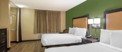 A hotel room with two beds, a desk, a chair, a lamp, and a mirror.