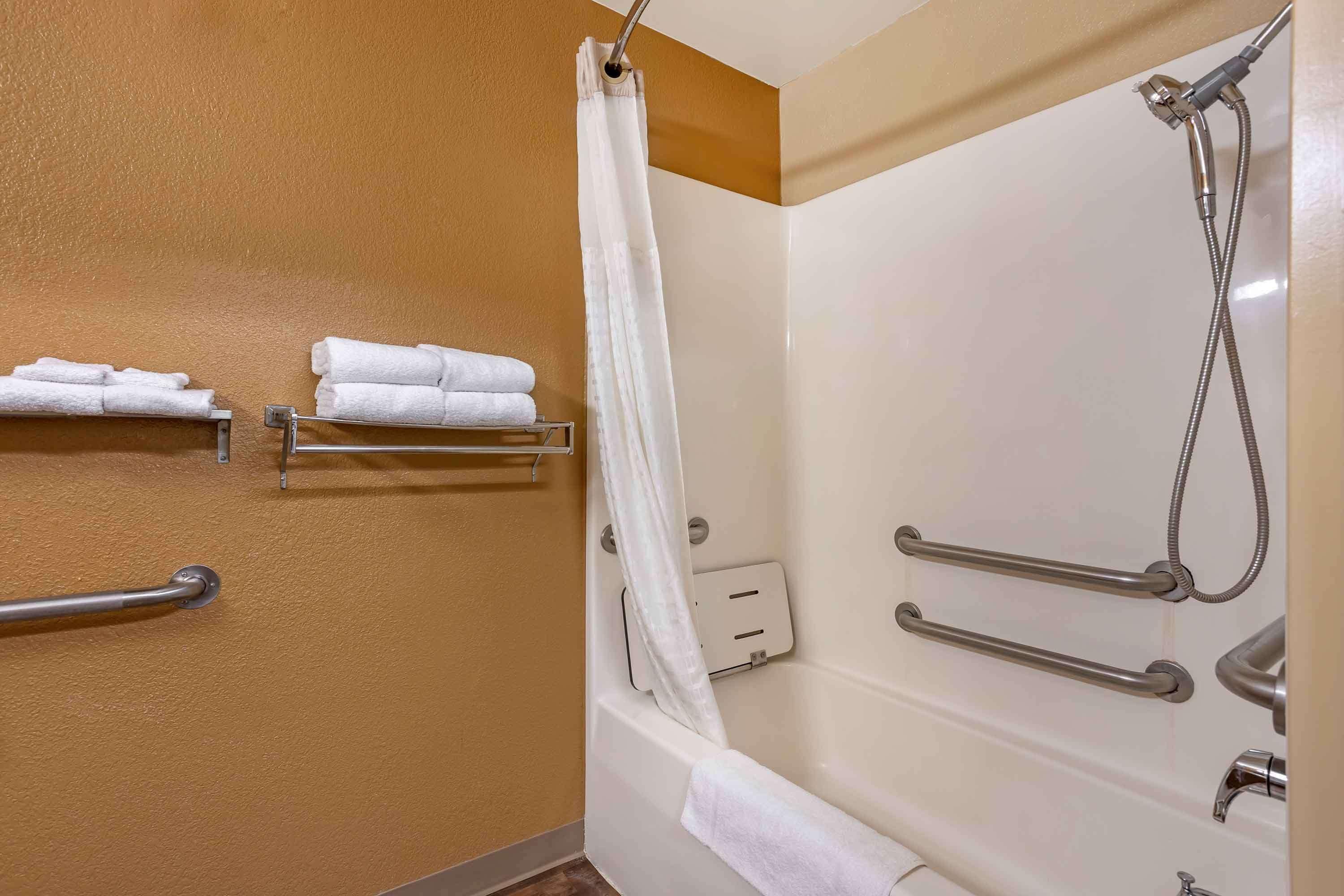 Une salle de bain équipée d’une baignoire, d’une douche et de barres d’appui. On y trouve des serviettes sur un porte-serviettes et un rideau de douche.