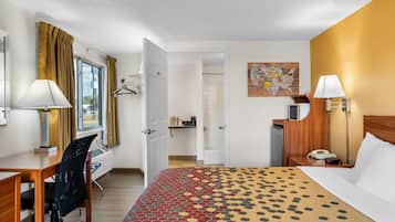 Une chambre d’hôtel avec un lit, un bureau, une chaise et une salle de bain visible à travers une porte ouverte.