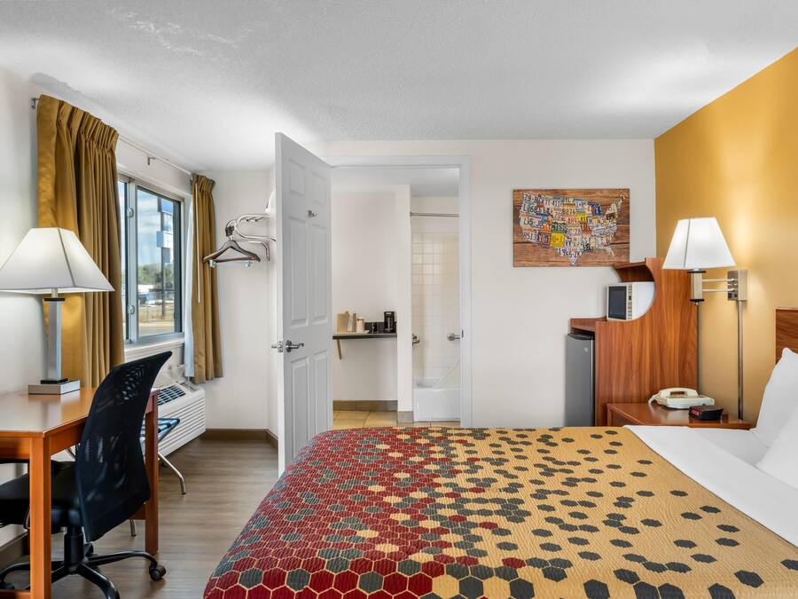 Une chambre d’hôtel avec un lit, un bureau, une chaise et une salle de bain visible à travers une porte ouverte.