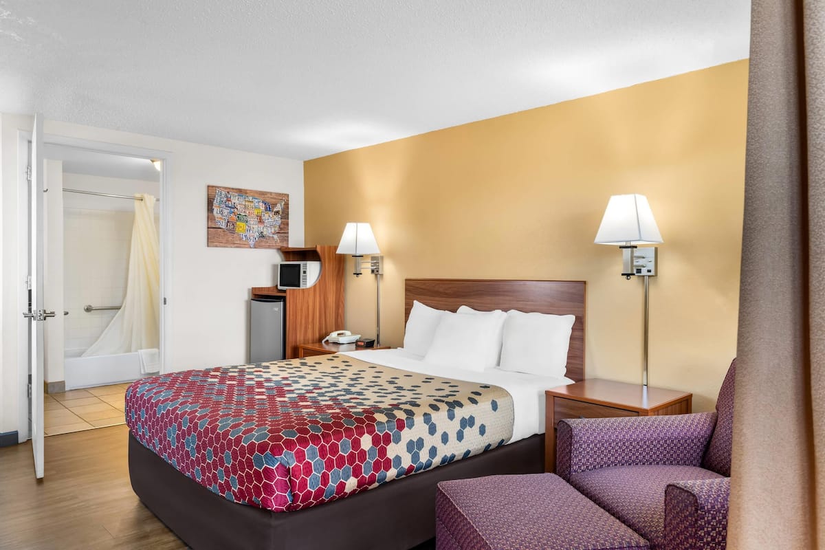 A hotel room with a bed, two bedside lamps, a desk, a chair, and a bathroom door.
