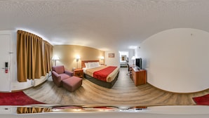 Et hotelværelse med buet loft, en seng med rødt sengetøj, et skrivebord med computer og et fjernsyn.