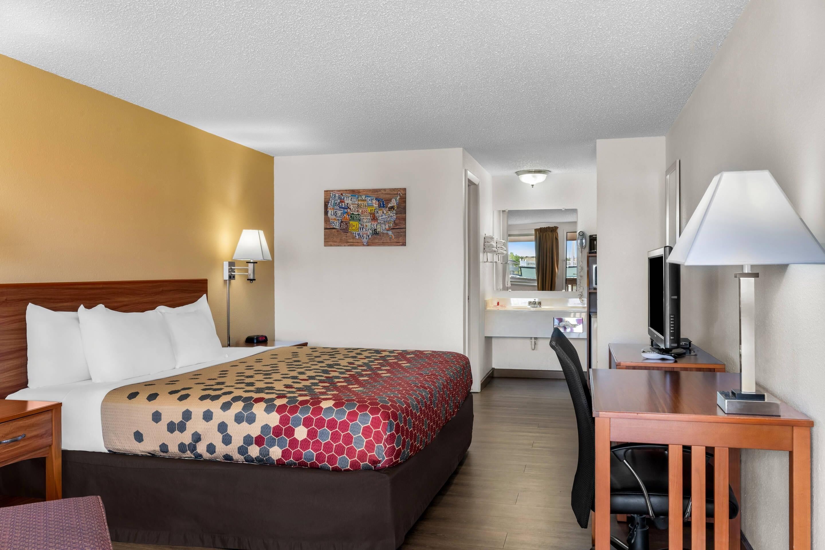 A hotel room with a bed, desk, chair, and a television.