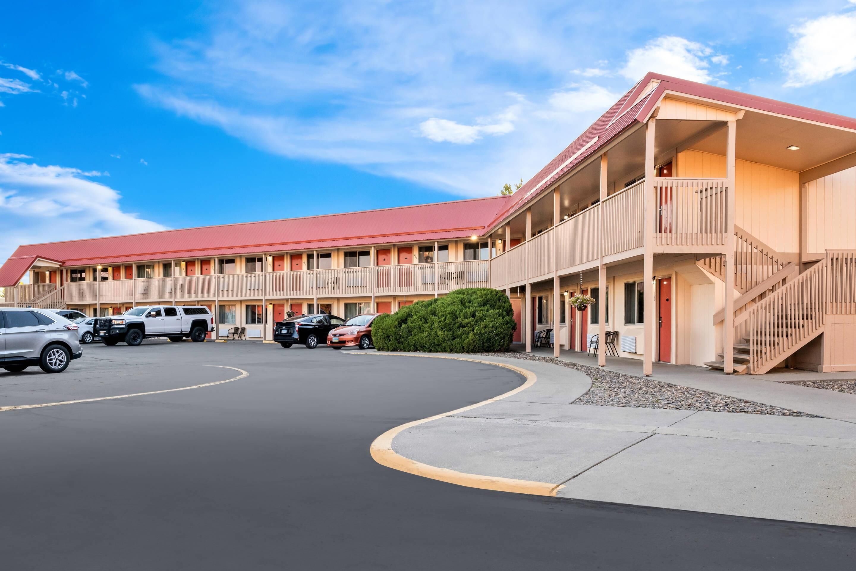 A motel with a red roof, multiple balconies, and a parking lot.