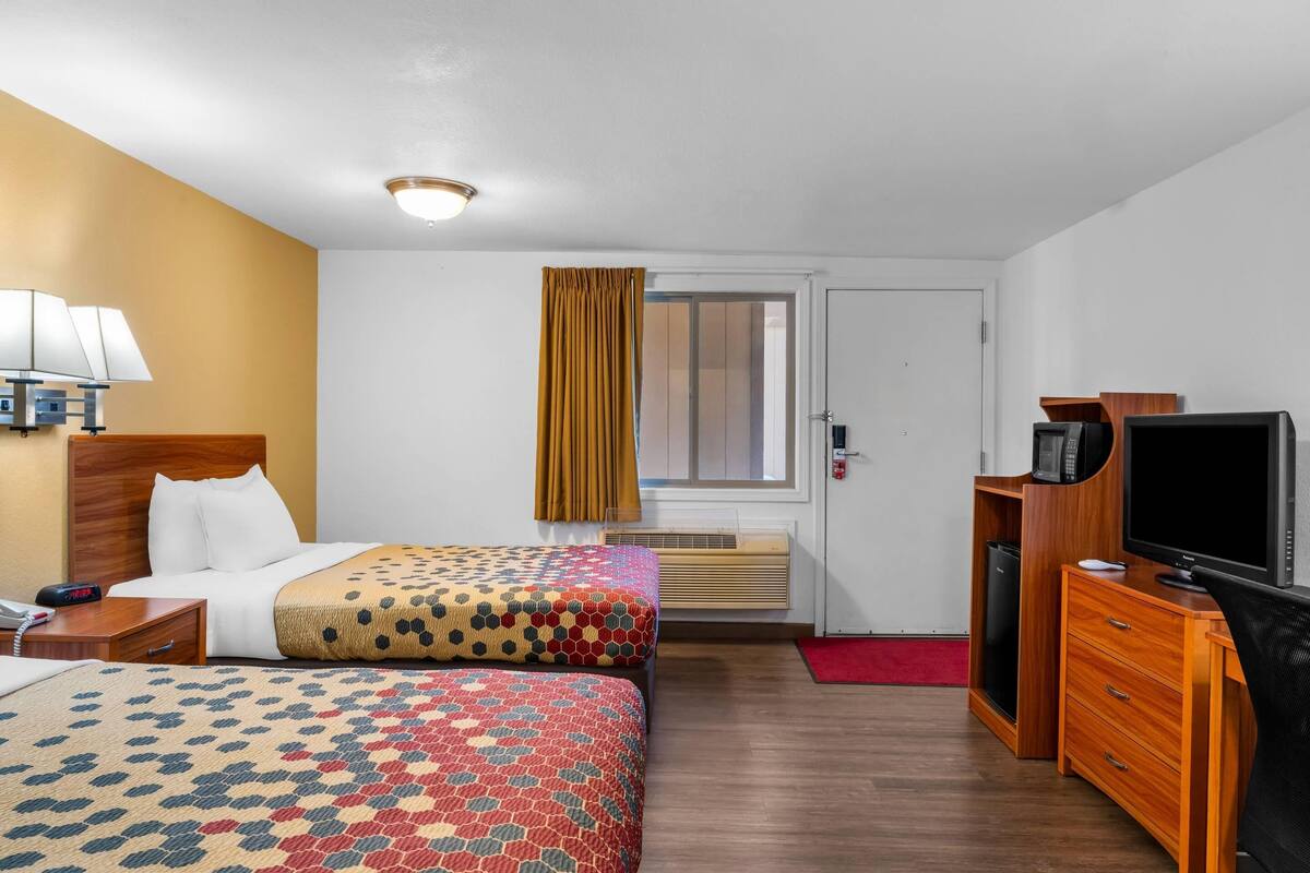 A hotel room with two beds, a desk with a TV, a lamp, and a window with curtains.