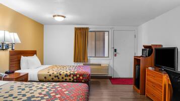 Ein Hotelzimmer mit zwei Betten, einem Schreibtisch, einem Fernseher, einer Lampe und einem Fenster mit Vorhängen.
