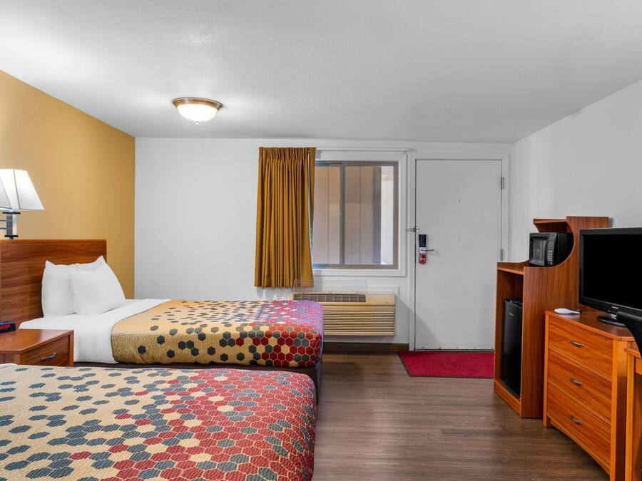 Ein Hotelzimmer mit zwei Betten, einem Schreibtisch, einem Fernseher, einer Lampe und einem Fenster mit Vorhängen.