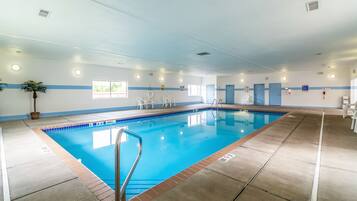 A large indoor swimming pool with clear lane markings, a lifeguard chair, and a potted plant.