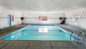 En indendørs swimmingpool med krystalklart vand, omgivet af vægge med blå striber og et loft med indbygningsbelysning.