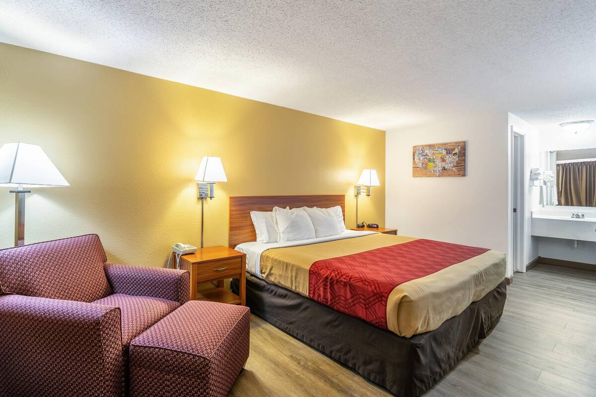A hotel room with a bed, two bedside tables, a chair, and a wall-mounted lamp.