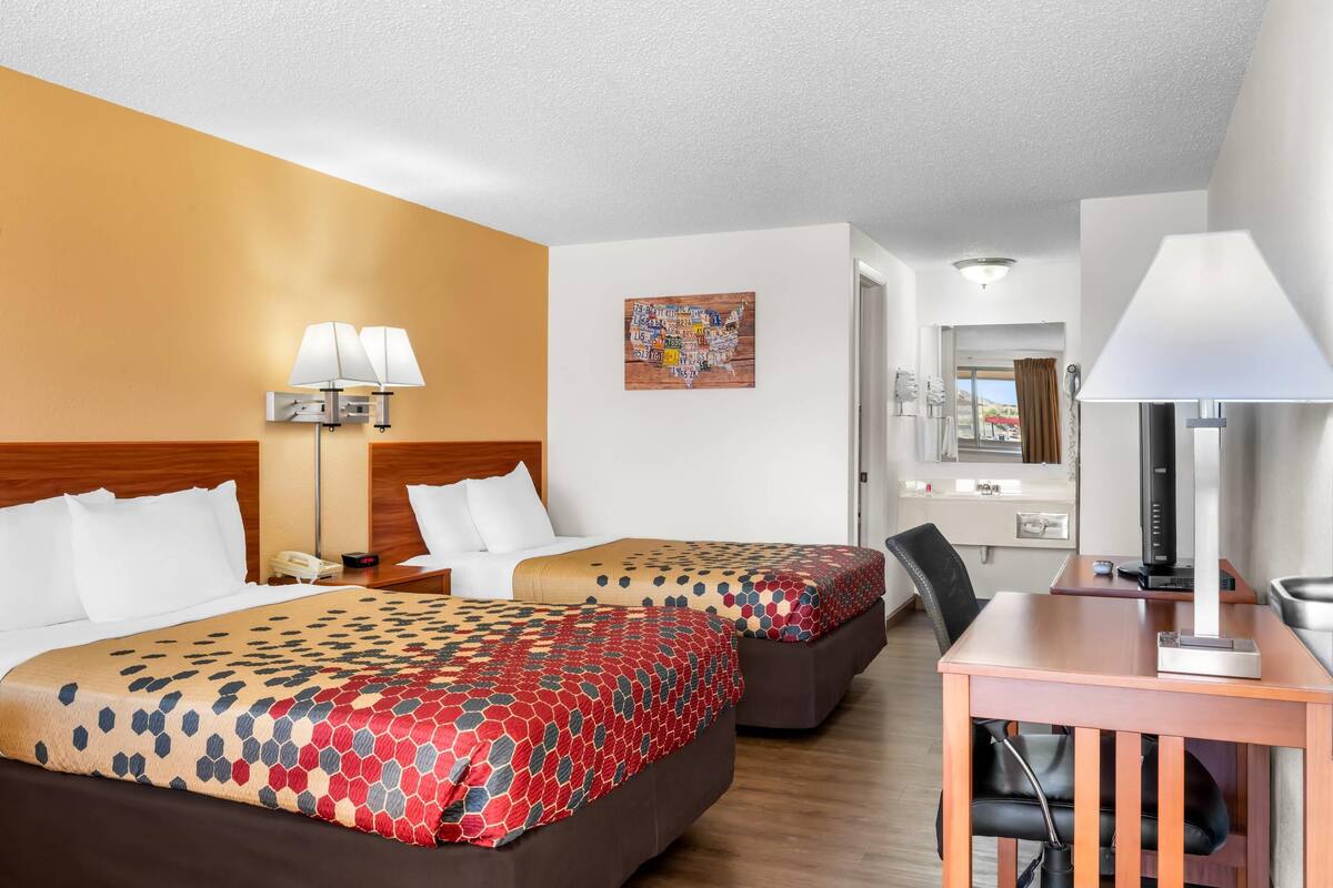 A hotel room with two beds, a desk, a computer, and a wall map.