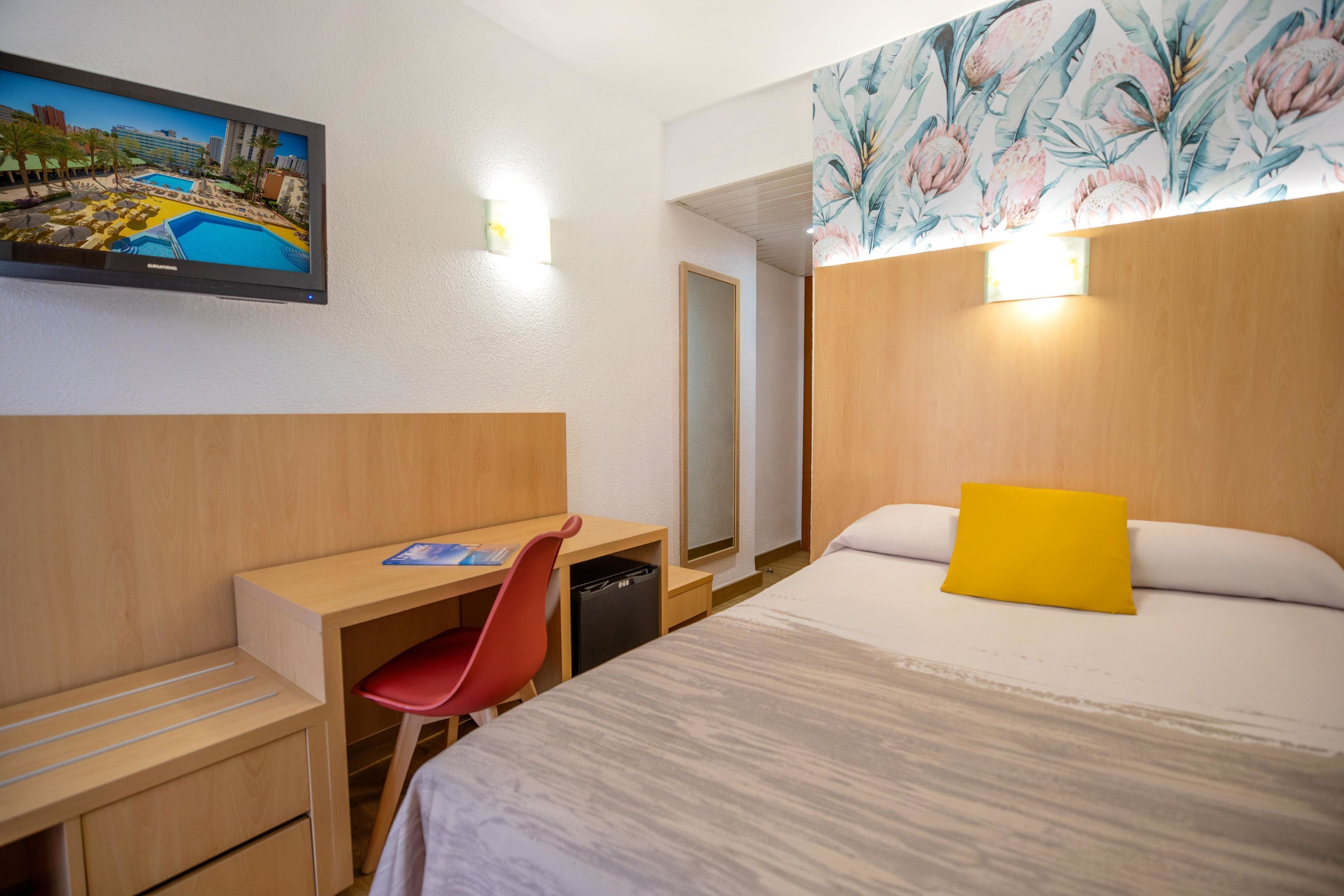 A hotel room with a bed, desk, chair, and a large mirror.