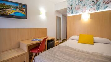 A hotel room with a bed, desk, chair, and a large mirror.