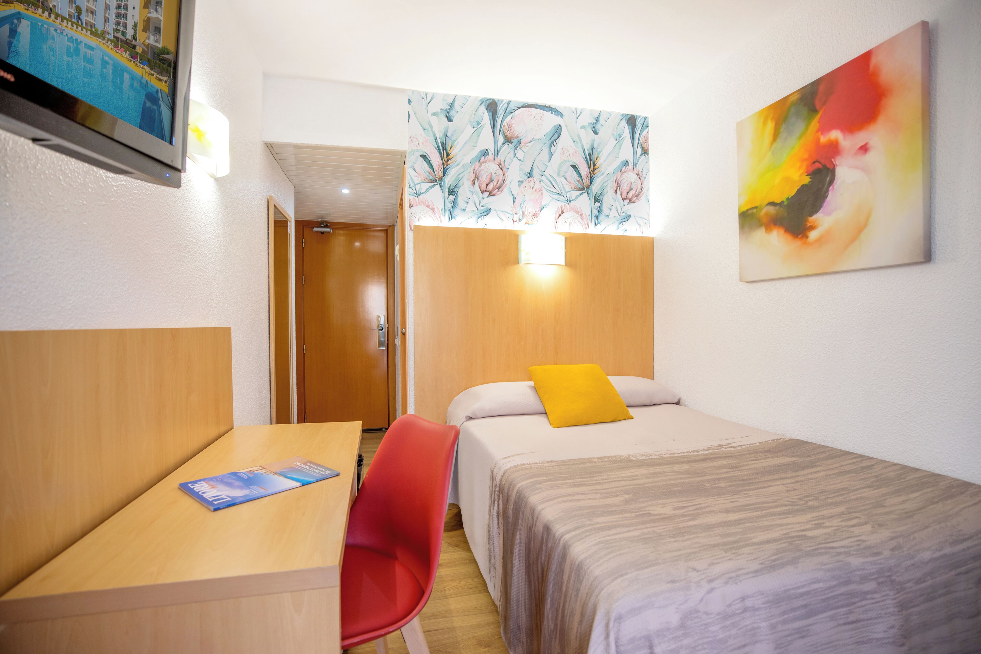 Habitación de hotel con cama, escritorio, silla, televisión y un cuadro en la pared.