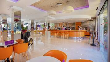 Un moderno vestíbulo de hotel con una zona de bar central, rincones de estar y un suelo limpio y pulido.